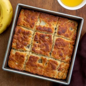 Pan of Banana Butter Swim Biscuits on a wooden table next to bananas and melted butter from overhead.