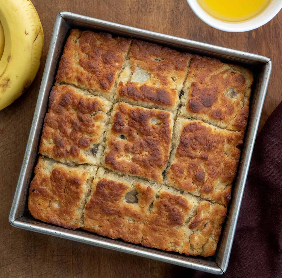 Pan of Banana Butter Swim Biscuits on a wooden table next to bananas and melted butter from overhead.