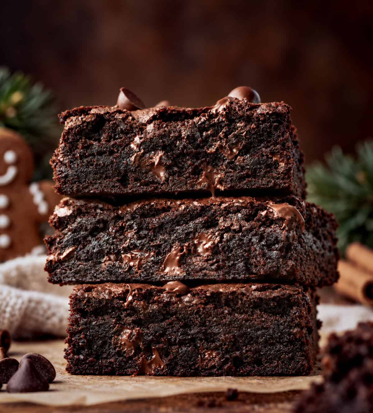 Stack of Chocolate Gingerbread Brownies on a wooden table with pine cones and evergreen needles.