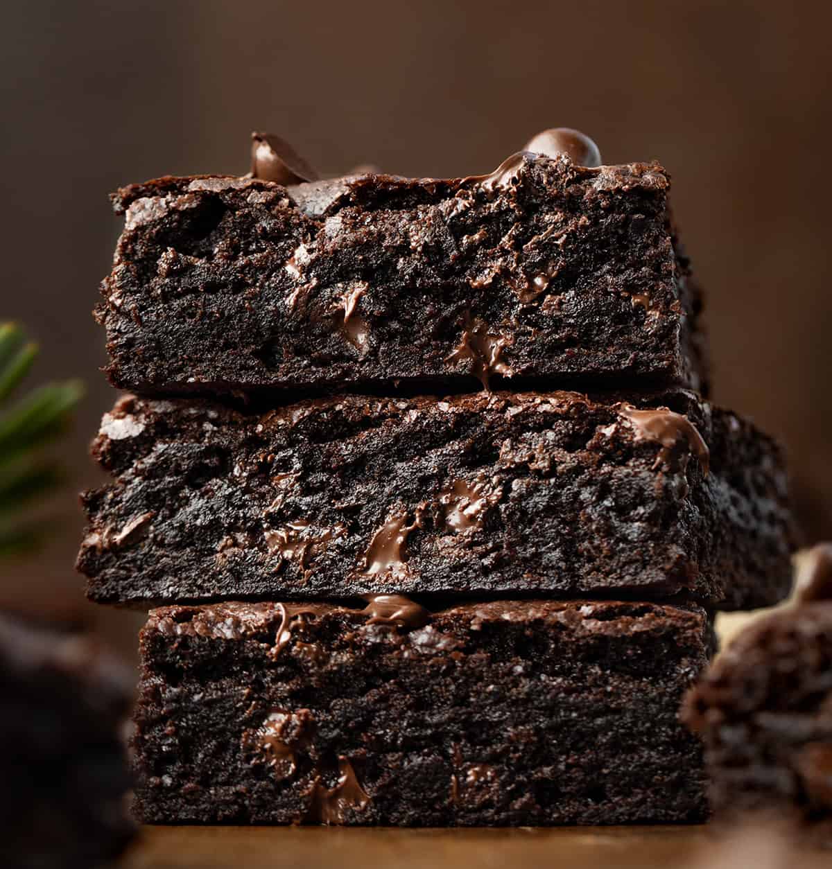 Stack of Chocolate Gingerbread Brownies on a wooden table with evergreen tree needles.