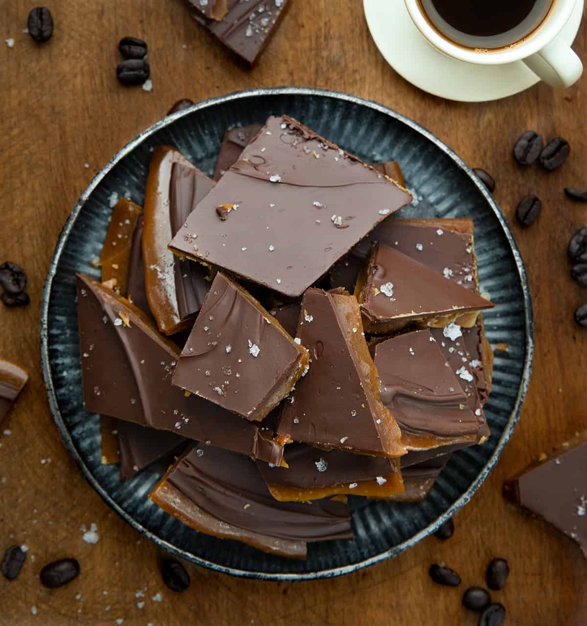 Platter of Coffee Toffee on a wooden table with a cup of coffee from overhead.