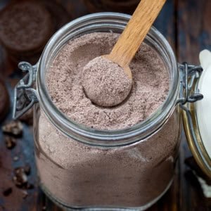 Big jar of Cookies & Cream Hot Cocoa Mix with a wooden measuring spoon in it.