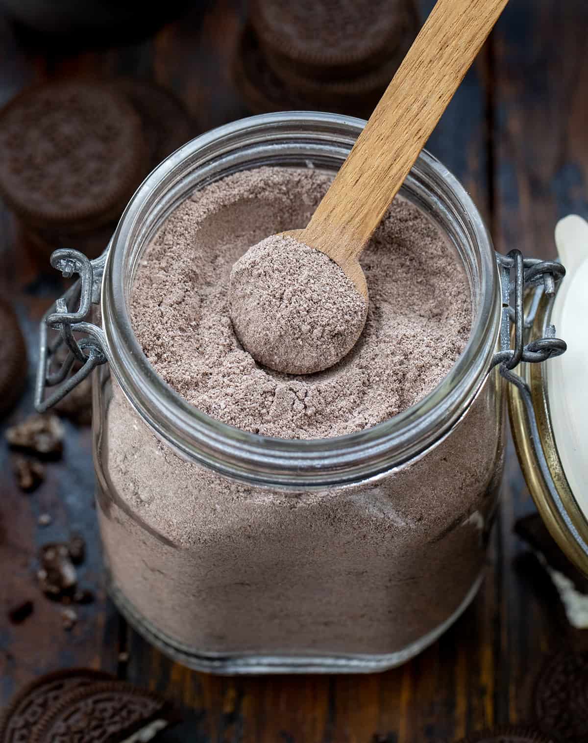 Big jar of Cookies & Cream Hot Cocoa Mix with a wooden measuring spoon in it.