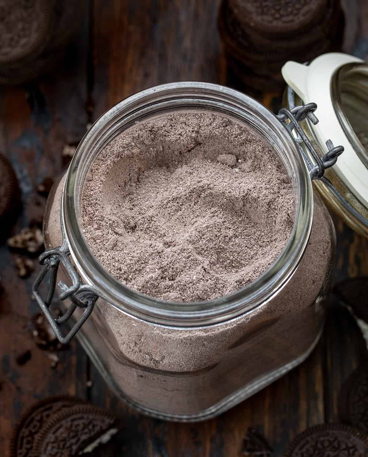 Looking down into a jar of Cookies & Cream Hot Cocoa Mix on a wooden table surrounded by Oreo's.