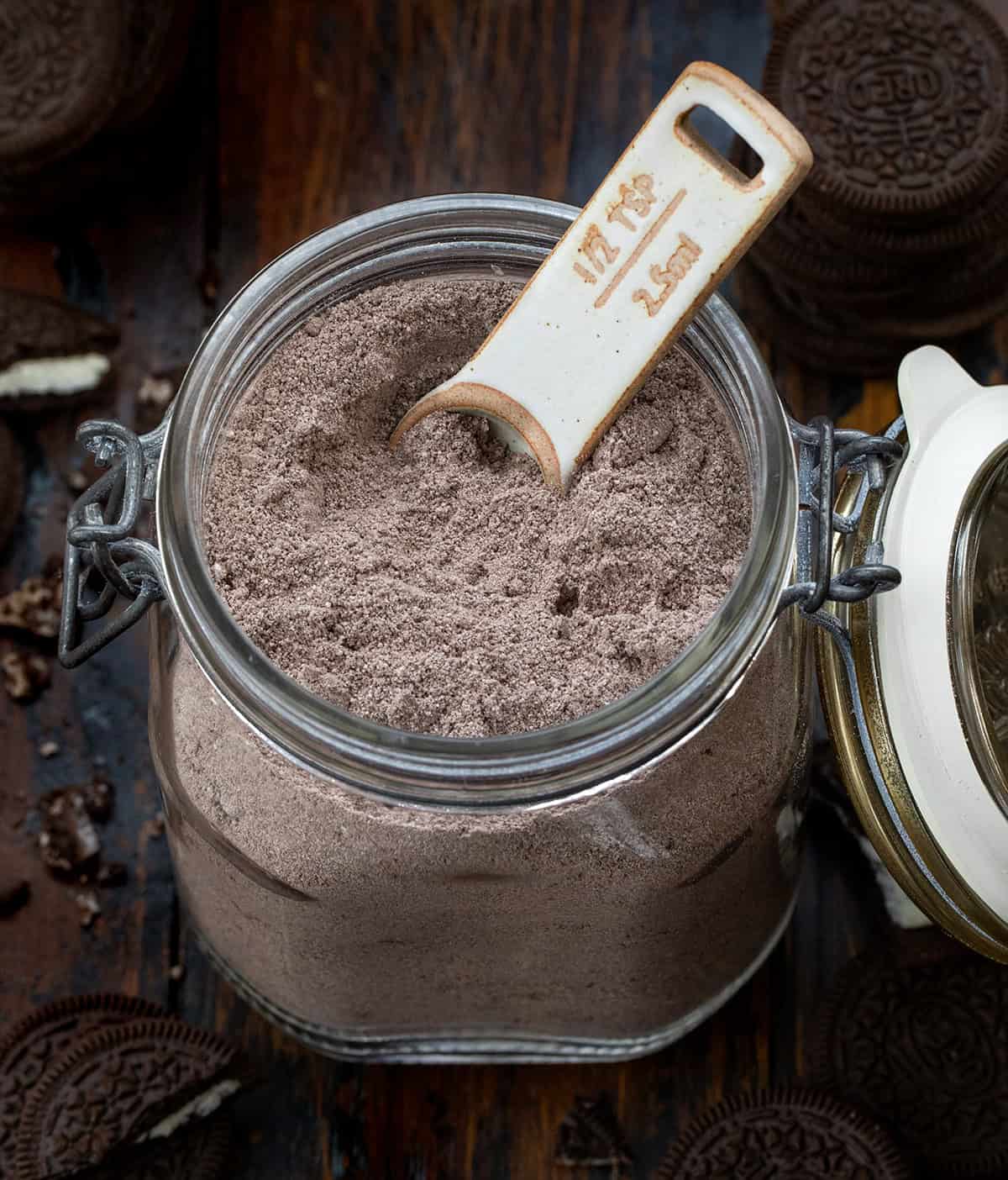 Mason jar of Cookies & Cream Hot Cocoa Mix with a measuring spoon in it on a wooden table.