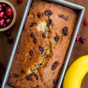 Loaf of Cranberry Banana Bread on a wooden table with fresh cranberries and bananas from overhead.