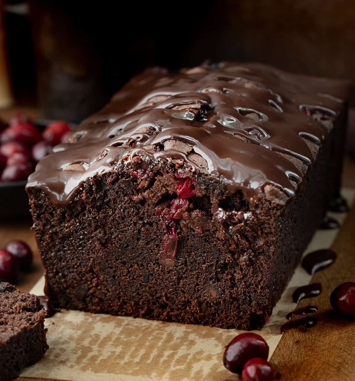 Loaf of cut into Cranberry Brownie Bread on a wooden table with cut slices and fresh cranberries.