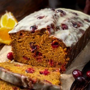 Cranberry Orange Pumpkin Bread with a few slices cut on a wooden table with fresh orange and cranberries.