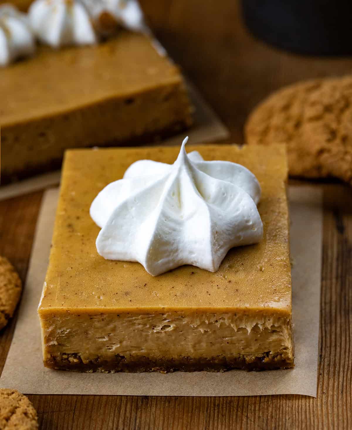 Gingerbread Cheesecake Bar squares on a wooden table with gingersnap cookies.