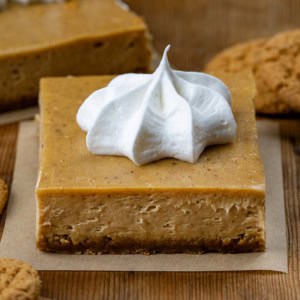 Gingerbread Cheesecake Bar squares on a wooden table with gingersnap cookies.
