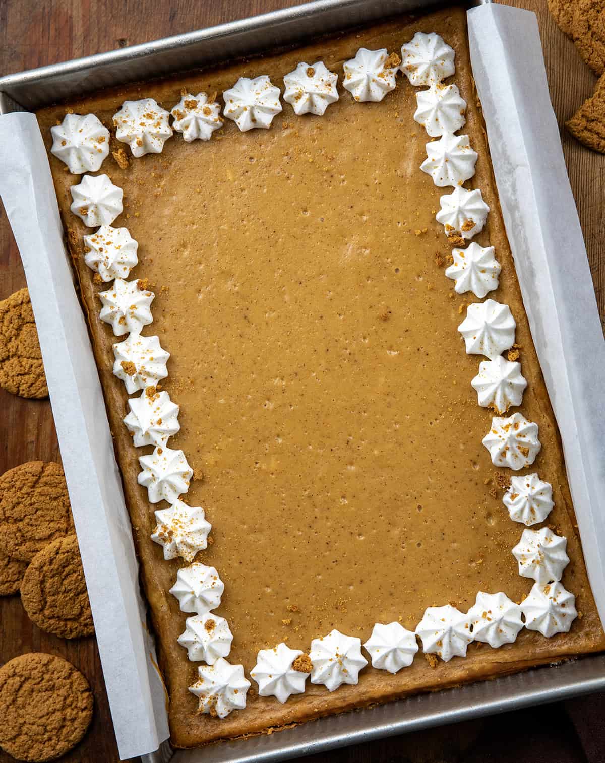 Pan of Gingerbread Cheesecake Bars decorated with whipped cream around the edge on a wooden table from overhead.