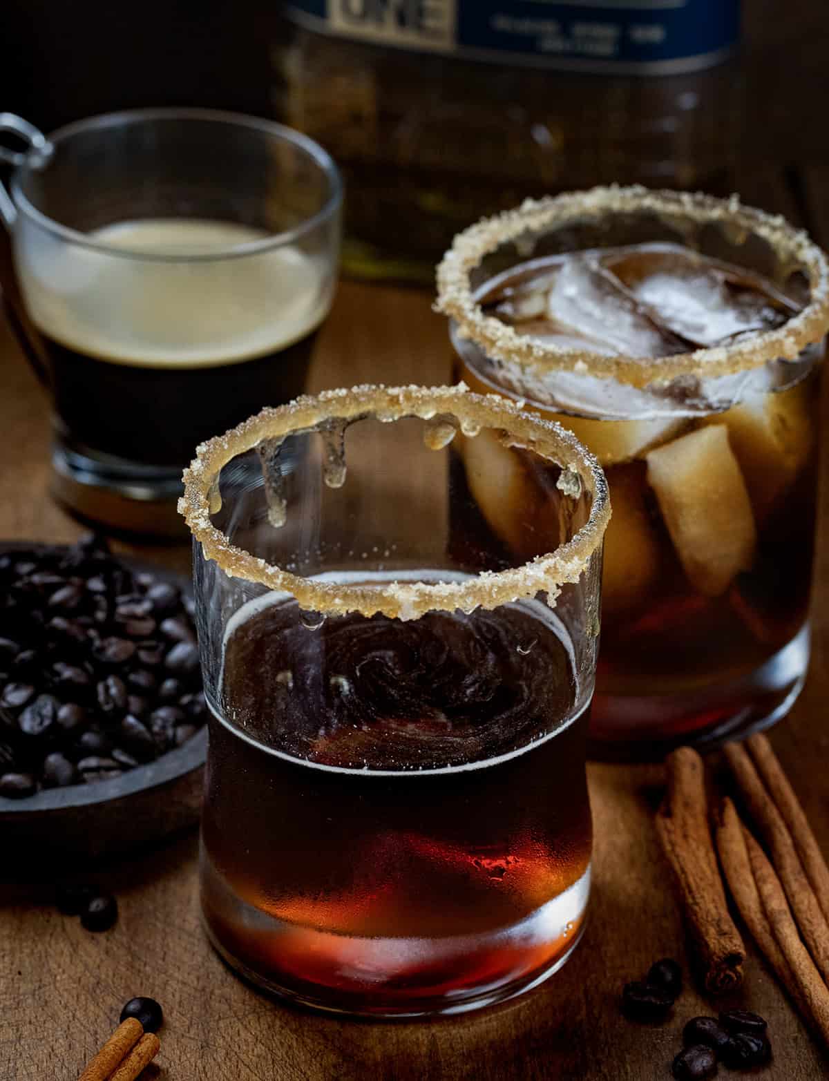 Glasses of Maple Bourbon Espresso and an espresso on a wooden table with coffee beans.