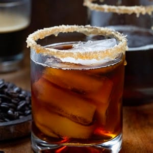 Glasses of Maple Bourbon Espresso on a wooden table with a glass of espresso and coffee beans.