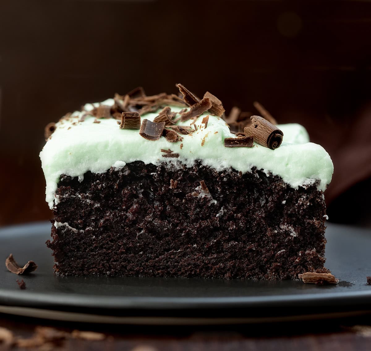 Close up of a piece of Mint Chocolate Sheet Cake on a black plate on a wooden table.