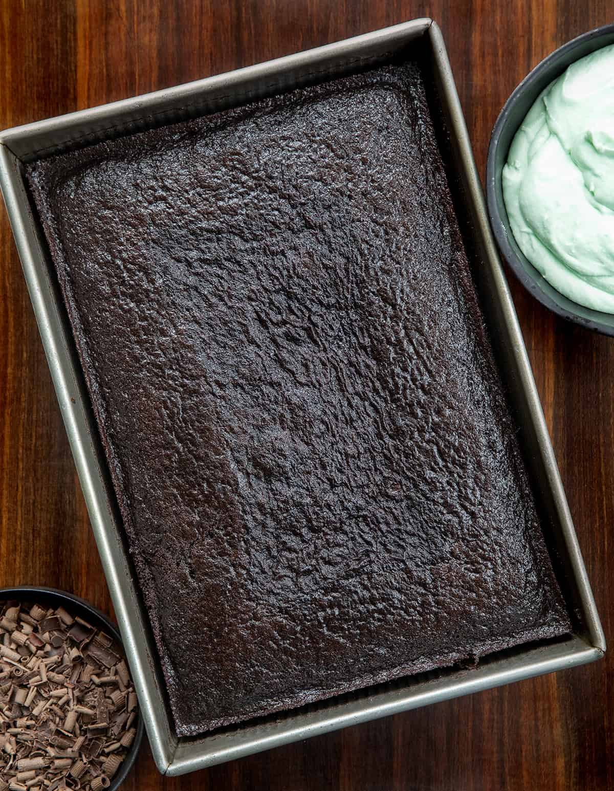 Chocolate sheet cake in the pan next to mint frosting and chocolate curls.