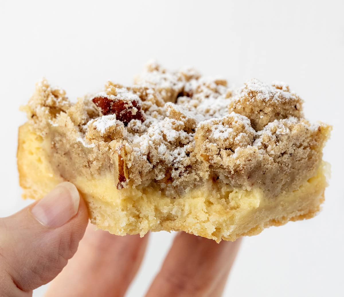 Hand holding a Pecan Vanilla Cream Crumb Bar with a bite taken out of it.
