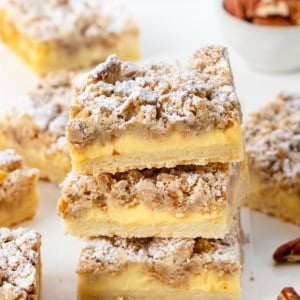 Stack of Pecan Vanilla Cream Crumb Bars surrounded by more bars and pecans.