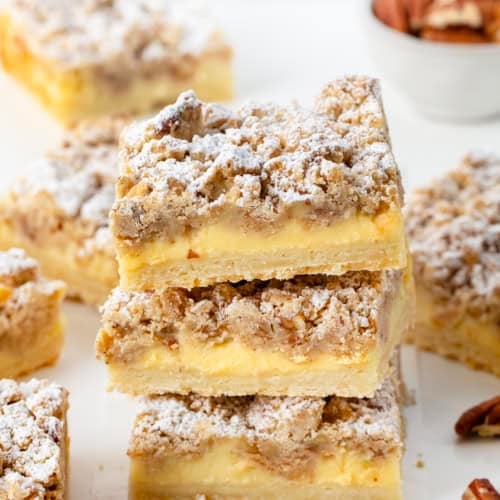 Stack of Pecan Vanilla Cream Crumb Bars surrounded by more bars and pecans.