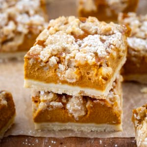 Small stack of Pumpkin Cream Crumb Bars on a wooden table surrounded by more bars.