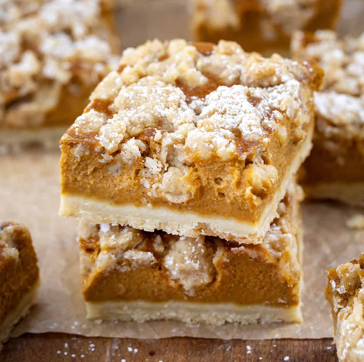 Small stack of Pumpkin Cream Crumb Bars on a wooden table surrounded by more bars.