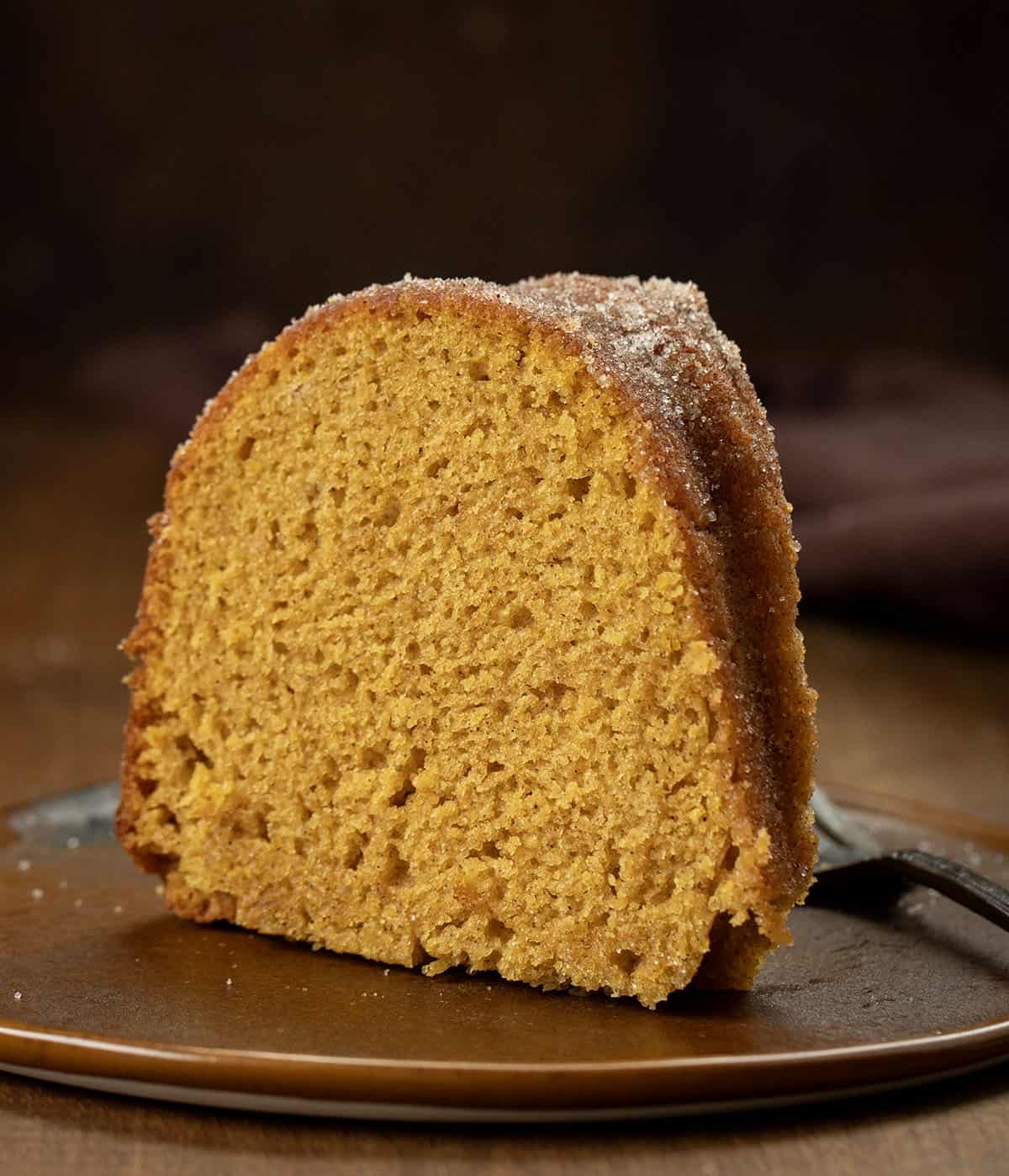 Slice of Pumpkin Spice Donut Bundt Cake on a brown plate on a wooden table.