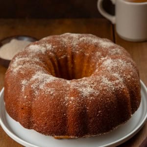 Pumpkin Spice Donut Bundt Cake on a wooden table with a cup of coffee.