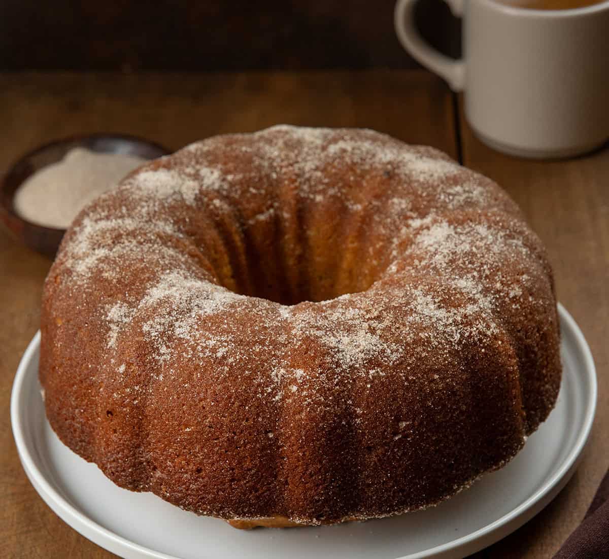 Pumpkin Spice Donut Bundt Cake on a wooden table with a cup of coffee.