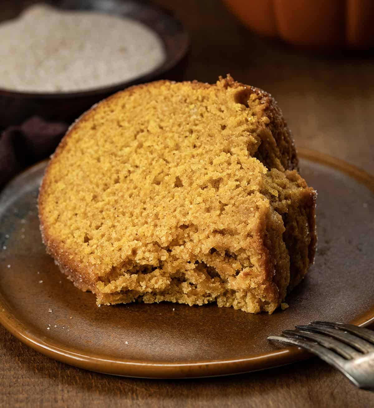 Slice of Pumpkin Spice Donut Bundt Cake with a bite taken out of it on a wooden table.