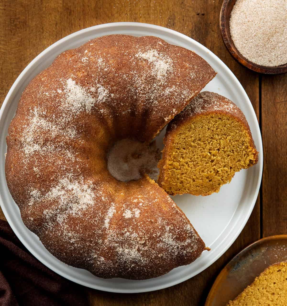 Cut into Pumpkin Spice Donut Bundt Cake with a slice laying on its side on a wooden table from overhead.